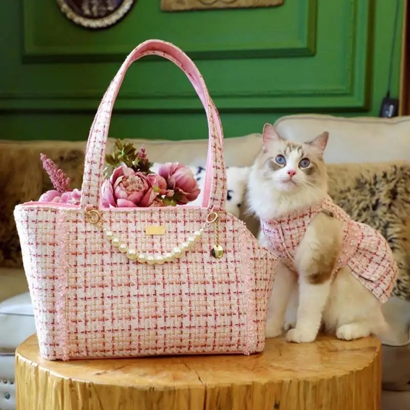 Cat in a pink dress sitting next to a pink handbag with flowers on a wooden table.