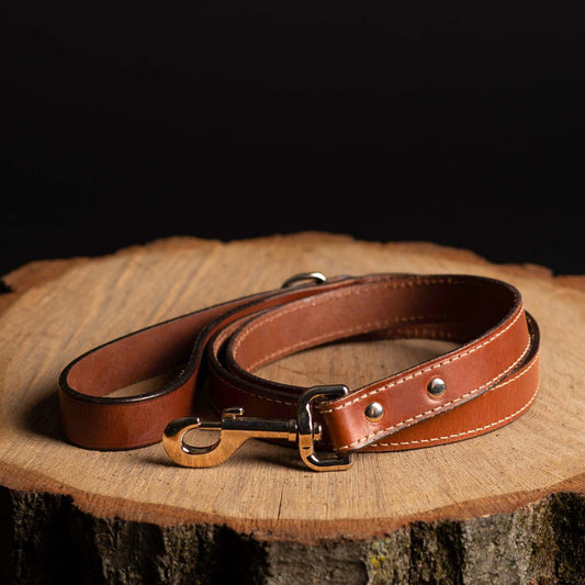 Brown leather dog leash with metal clip on a wooden surface
