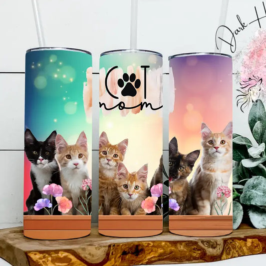 Three colorful tumblers with cat-themed designs on a wooden surface.