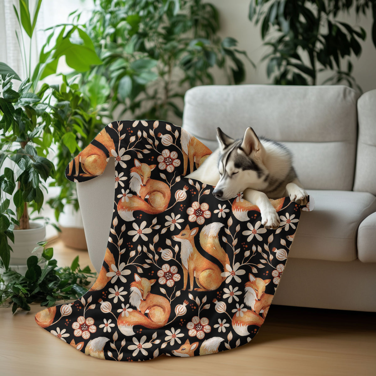 Dog lying on a floral-patterned blanket with foxes and flowers, surrounded by plants and a couch.