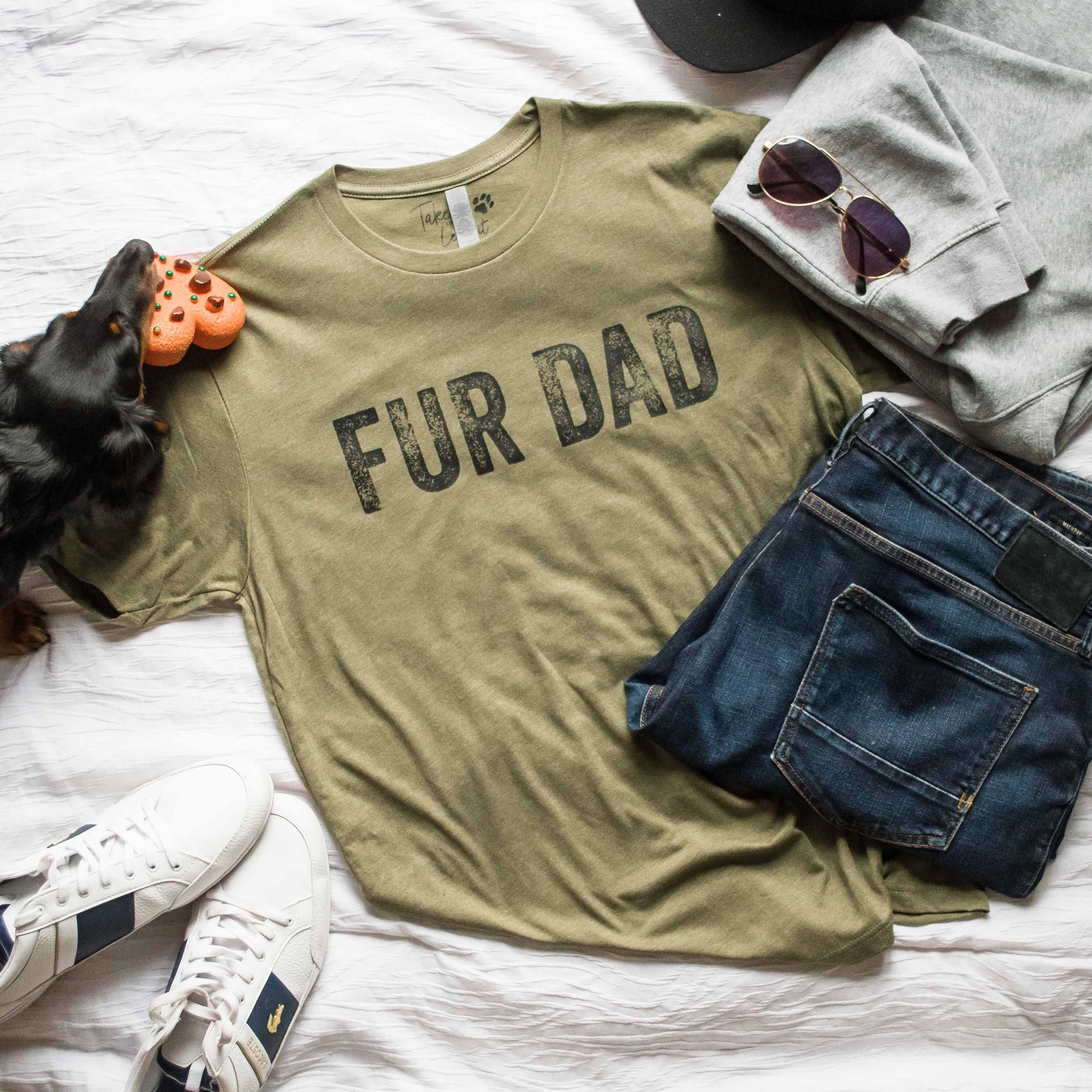 Green t-shirt with 'FUR DAD' text on a bed with jeans, sneakers, and a dog toy.