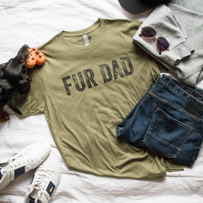 Green t-shirt with 'FUR DAD' text on a bed with jeans, sneakers, and a dog toy.