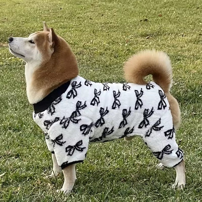 Dog wearing a white coat with black bow patterns on a grassy field