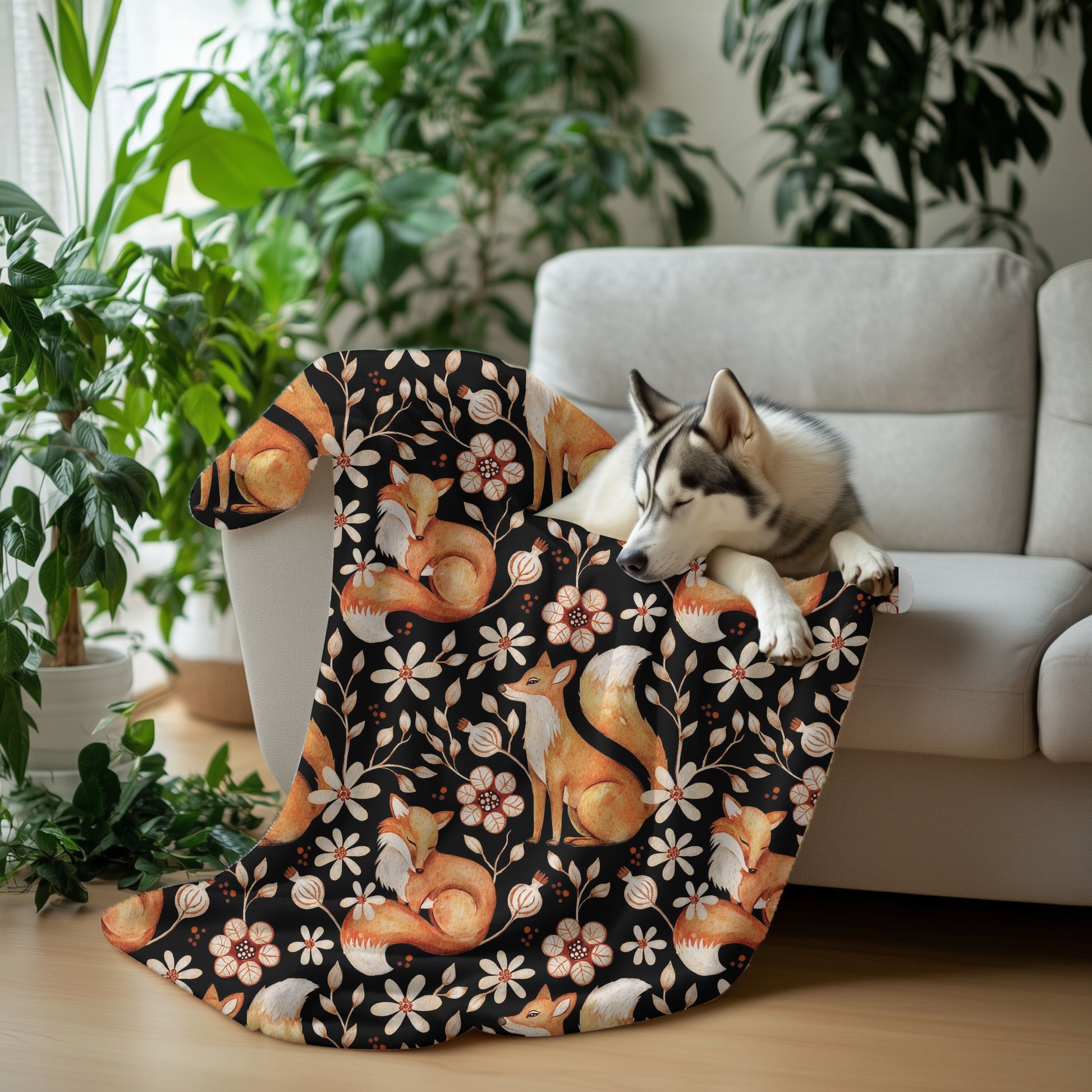 Dog lying on a floral-patterned blanket with foxes and flowers, surrounded by plants and a couch.