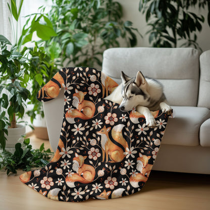 Dog lying on a floral-patterned blanket with foxes and flowers, surrounded by plants and a couch.