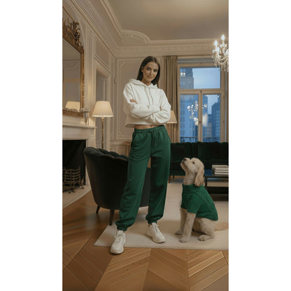 Woman in white hoodie and green pants standing in a stylish room with a dog wearing a matching outfit.