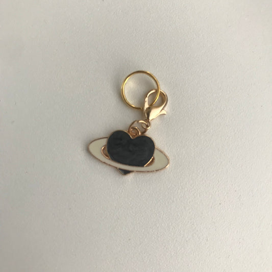 A small gold-tone charm shaped like a black heart with a white ring, attached to a gold key ring and lobster clasp, photographed on a plain light background.