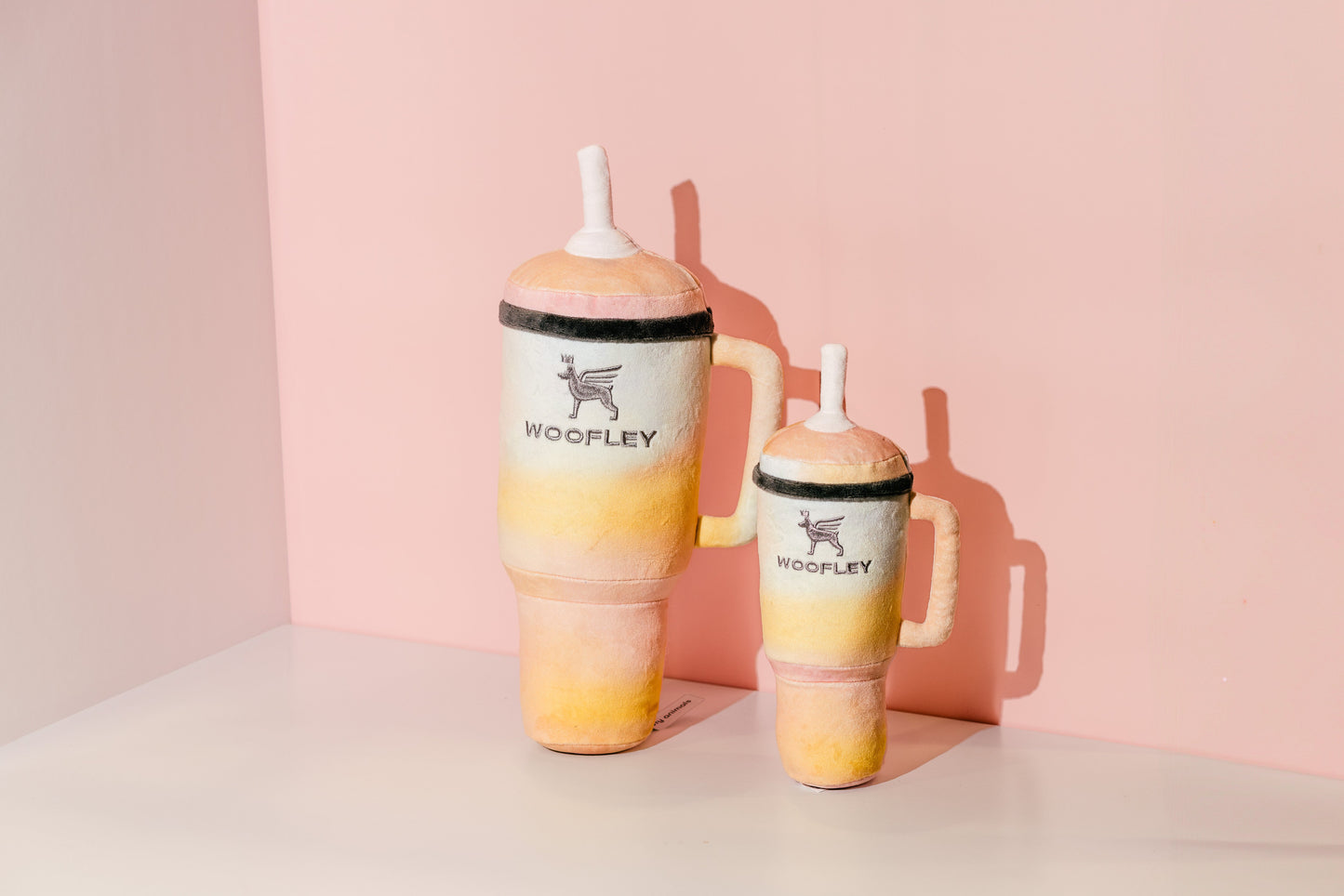 Two gradient tumbler mugs with 'Woofley' branding on a pink background