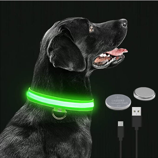 A black dog wearing a luminous green LED dog collar with a USB charging cable and a button remote control.